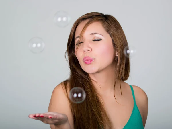 Woman blowing some soap bubbles, closed eyes and extended hand, gray background — Stock Photo, Image