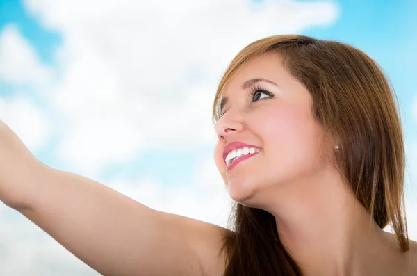 Close up van gezicht vrouw met haar arm verlengd, glimlachend met een hemelachtergrond — Stockfoto