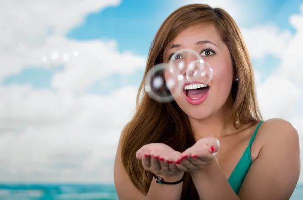 Woman surprised with soap bubbles, trying to catch them in her hands, sky background — Stock Photo, Image