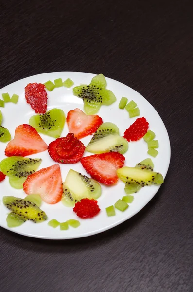 Sliced kiwi and strawberries lying in neatly placed pattern on white plate, as senn from above — Stock Photo, Image