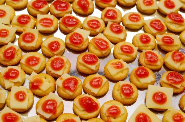 Plateau de biscuits au fromage et garniture rouge, alignés sur une surface métallique — Photo