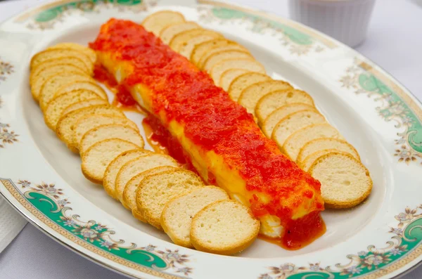 Fette di baguette tostate sottili e croccanti impilate su un piatto bianco con salsa rossa e formaggio al centro — Foto Stock