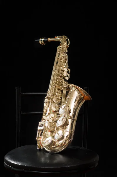 Beau saxophone doré debout sur une chaise avec tout le fond noir — Photo