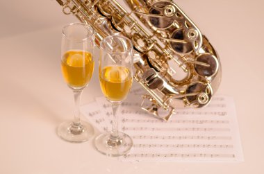 Parlak saksafon beyaz yüzey, müzik notaları kağıt ve şampanya yanında oturan iki bardak yalan