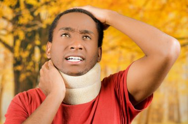 Boyunluk giyen yaralı genç pozitif siyah İspanyol erkek, ağrı etrafında el ele tutuşarak acı yüzleri yapma destek, sarı soyut arka plan