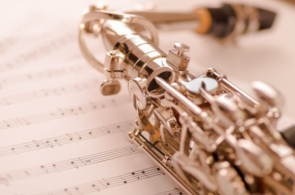 Closeup partly view of shiny saxophone lying on musical notes paper