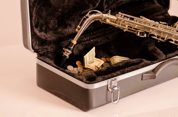 Блестящий саксофон лежит на открытой инструментальной оболочке с черным бархатным интерьером и кучей денег внутри — стоковое фото