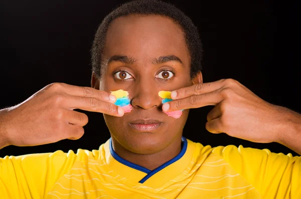 Headshot koyu tenli erkek siyah arka plan önünde sarı futbol gömlek giyen, yanaklara facepaint uygulayarak parmakları kullanarak — Stok fotoğraf