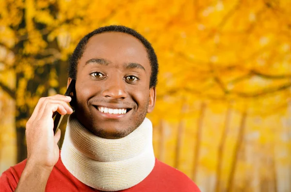 Varón hispano negro positivo joven lesionado con corsé en el cuello y sonriendo a la cámara, fondo abstracto amarillo —  Fotos de Stock