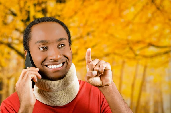 Verletzter junger positiver schwarzer hispanischer Mann trägt Nackenstütze und telefoniert lächelnd, gelber abstrakter Hintergrund — Stockfoto