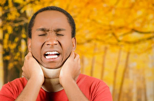 Geblesseerd jonge positieve zwarte Spaanse mannelijke dragen nek brace, handen vasthouden in pijn rond ondersteuning maken gezichten van Agony, gele abstracte achtergrond — Stockfoto