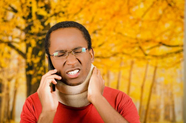 Skadade unga positiva Svarta spansktalande manliga bär nack stag, talar på telefon och hand hålla stöd i ångest, gul abstrakt bakgrund — Stockfoto