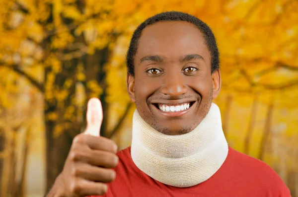 Varón hispano negro positivo joven lesionado con corsé en el cuello y sonriendo a la cámara dando pulgar hacia arriba, fondo abstracto amarillo — Foto de Stock