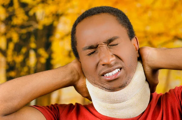 Varón hispano negro lesionado con corsé en el cuello, cogido de la mano con dolor alrededor de apoyo haciendo caras de agonía, fondo abstracto amarillo —  Fotos de Stock