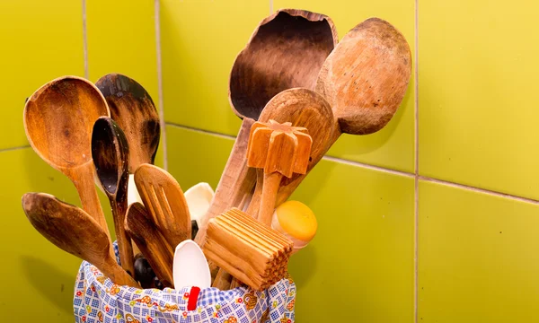 Varias espátulas de madera bien utilizadas y otras herramientas de cocina que sobresalen de la taza de almacenamiento, fondo de azulejos verdes — Foto de Stock