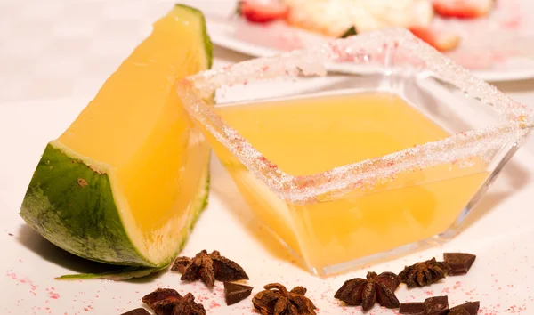 Square transparent bowl with sugarcoating around edges and yellow liquid inside nexto to melon — Stock Photo, Image