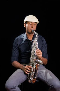 Beyaz şapka ile siyah bir adam oturuyor ve oynarken onun saksafon, koyu arka plan, güzel müzik