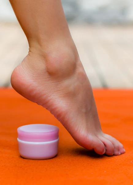 Schöne Füße stehen auf ihren Zehen mit einem Topf mit Creme, rosa Farbe des Topfes und orangefarbenem Hintergrund — Stockfoto