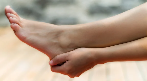 เท้าผู้หญิงที่สะอาดและมือขวาของเธอสัมผัสส้นเท้าของเธอพื้นหลังของไม้และหิน — ภาพถ่ายสต็อก