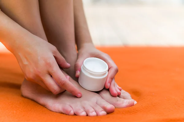 Vrouw het maken van haar voeten prachtig, apllying sommige hydraterende crème met haar handen, oranje achtergrond — Stockfoto