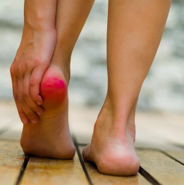 Red heel because of pain, woman hand making some massage. Wooden floor — Stock Photo, Image