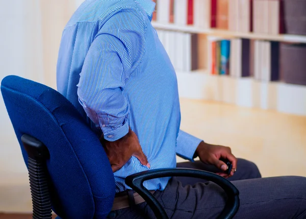 Mann sitzt auf einem Stuhl, legt die Hand auf den Rücken, Schmerzsignal — Stockfoto