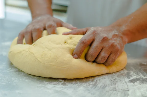 Пекари руками работают и месят большое хлебное тесто на металлической поверхности с разбросанной мукой — стоковое фото
