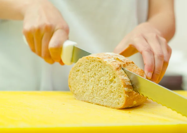 Tagliare le fette di pane seduto su una superficie gialla, tenendo in mano un coltello grande — Foto Stock