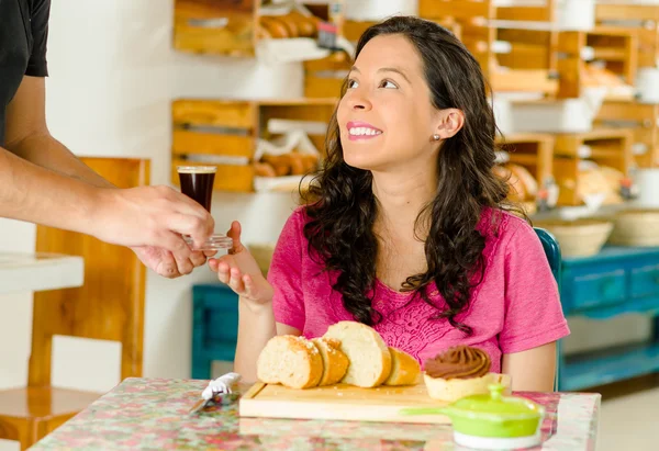 Hübsche brünette Frau sitzt am Tisch in der Bäckerei, bekommt Espressomaschine vom Kellner und lächelt glücklich — Stockfoto