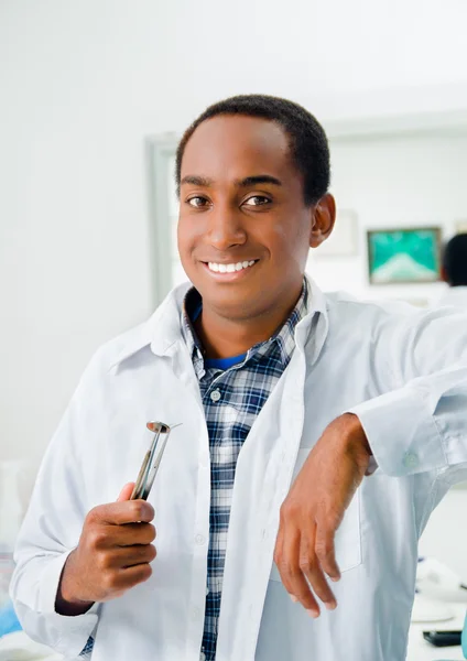 Handsome hispanic dentist wearing white doctors coat and holding dental tool while smiling posing to camera — Stock Photo, Image