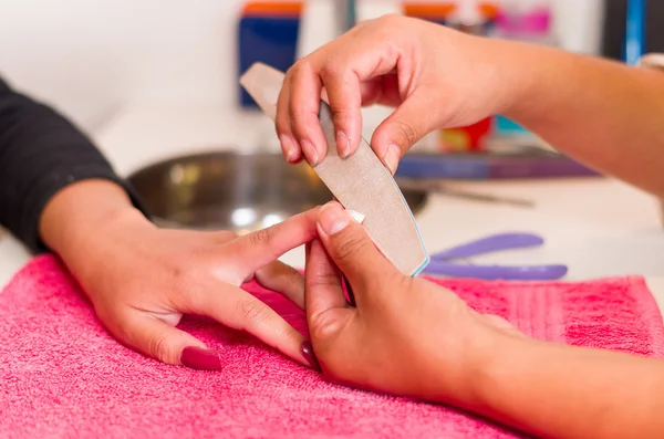 Primo piano le mani delle donne ottenere un trattamento di manicure da donna in ambiente salone, superficie di tovagliolo rosa, prodotti di sfondo sfocati — Foto Stock