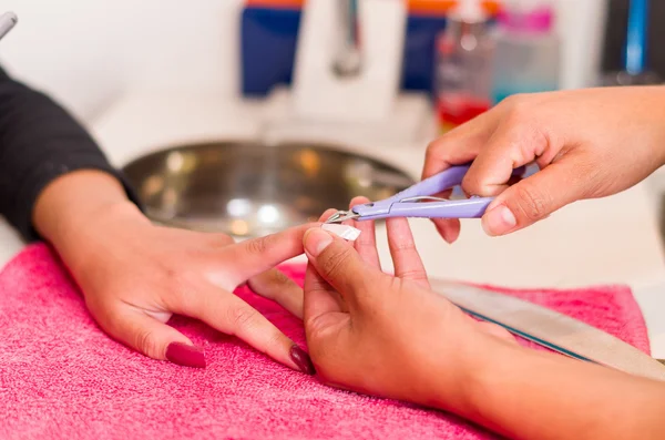 Closeup females hands getting manicure treatment from woman using nail scissors in salon environment, pink towel surface, blurry background products — Stock Photo, Image