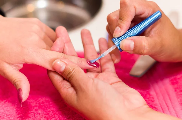 Closeup females hands getting manicure treatment from woman using small brush in salon environment, pink towel surface, blurry background products — Stock Photo, Image
