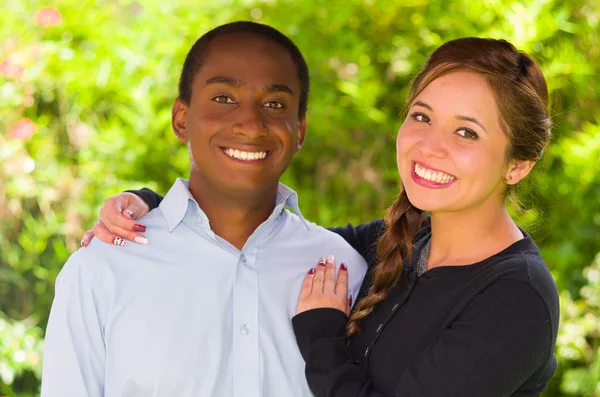 Bela jovem casal interracial no ambiente do jardim, abraçando e sorrindo feliz para a câmera — Fotografia de Stock