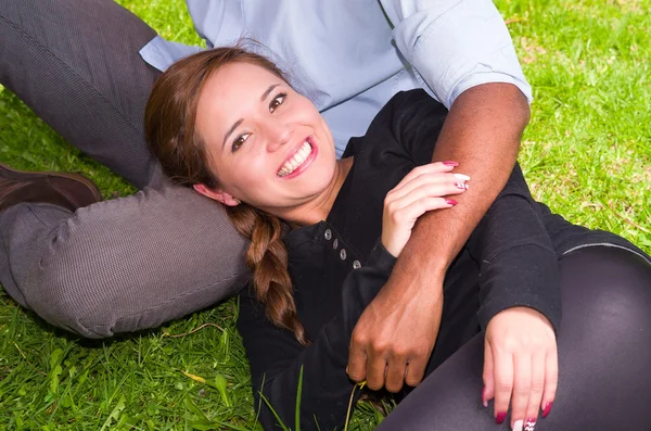 Bela jovem casal interracial no ambiente de jardim sentado, abraçando e sorrindo alegremente para a câmera — Fotografia de Stock