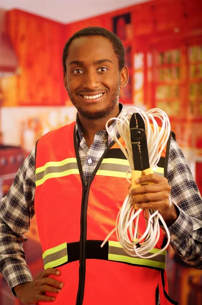Young electrical worker wearing safety vest, holding cables and cable pliars, smiling with great positive attitude