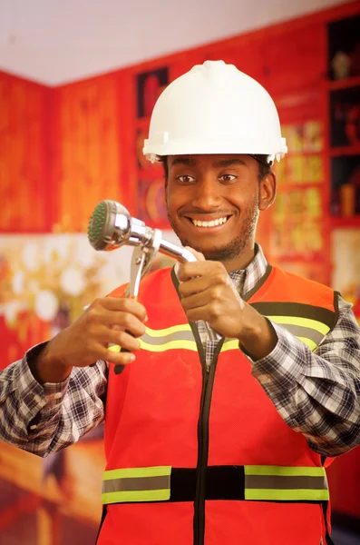Young engineer wearing square pattern flanel shirt with red safety vest, holding showerhead and pliars smiling to camera — Stock Photo, Image