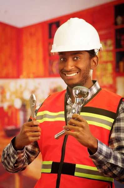 Young engineer wearing square pattern flanel shirt with red safety vest, holding showerhead and pliars smiling to camera — Stock Photo, Image