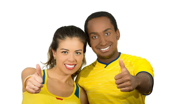 Чарівна міжрасова пара в жовтих футбольних сорочках, що дає великі пальці на камеру, білий студійний фон — стокове фото