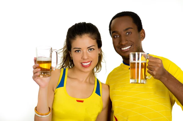 Encantadora pareja interracial con camisas de fútbol amarillo, posando para la cámara sosteniendo gafas de cerveza y sonriendo, fondo de estudio blanco —  Fotos de Stock