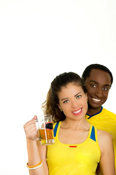 Encantadora pareja interracial con camisas de fútbol amarillo, posando para la cámara sosteniendo un vaso de cerveza y sonriendo, fondo de estudio blanco —  Fotos de Stock