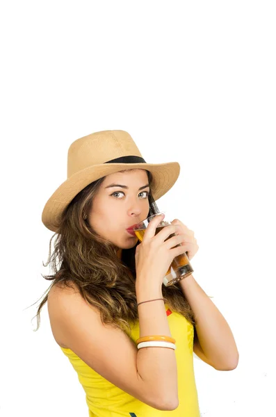 Morena hispana vistiendo camiseta de fútbol amarillo y sombrero, posando para la cámara mientras bebe de un vaso de cerveza, fondo blanco del estudio — Foto de Stock