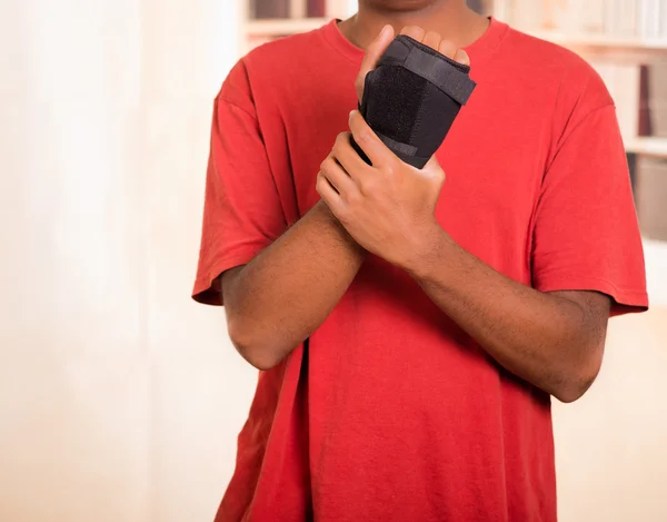 Man in red shirt wearing black wrist brace support on right hand and gripping arm with other — Stock Photo, Image