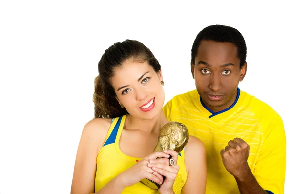 Encantadora pareja interracial con camisas de fútbol amarillo sosteniendo pequeño trofeo posando para la cámara, fondo de estudio blanco — Foto de Stock