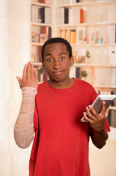 Man in red shirt wearing large grey bandage over lower right arm, holding tablet in other hand and looking into camera — Stock Photo, Image