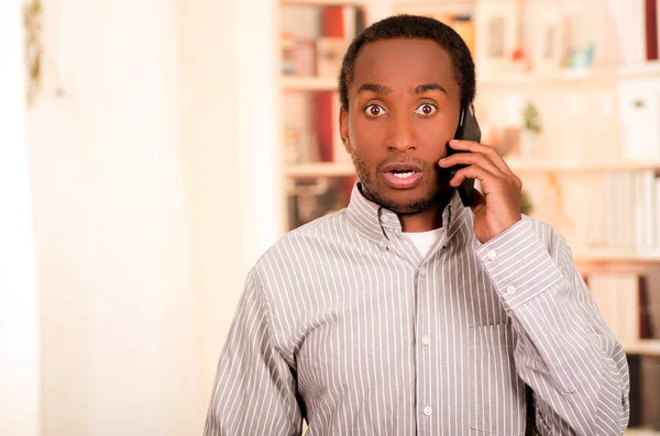 Hombre guapo con ropa casual hablando en el teléfono móvil mientras apunta hacia arriba, fondo blanco estanterías — Foto de Stock