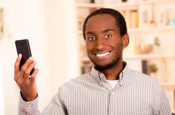 Hombre guapo con ropa casual sosteniendo el teléfono móvil mirando a la cámara y sonriendo — Foto de Stock
