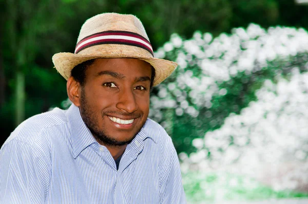 Bell'uomo che indossa camicia blu e cappello estivo sorridente mentre si gode una bella giornata nell'ambiente del parco — Foto Stock