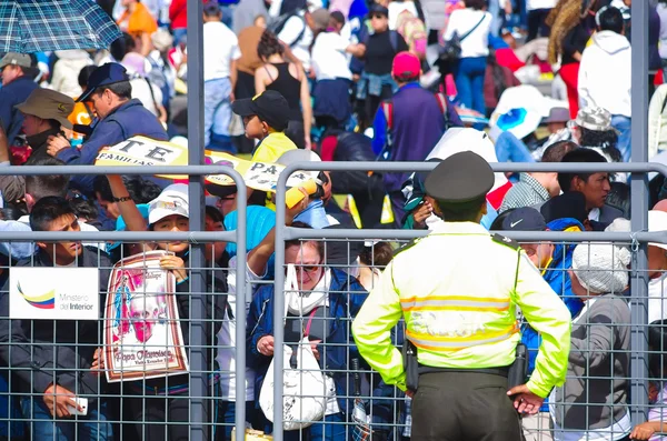 QUITO, ECUADOR - JULY 7, 2015: Polisi menjaga pantai orang-orang di misa Paus Francisco, poster dan orang-orang di balik jala logam — Stok Foto