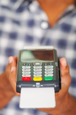 Kamera önünde kredi kartı ödeme terminalini tutan mavi beyaz kare desenli gömlek giyen adam, yakın çekim açısı